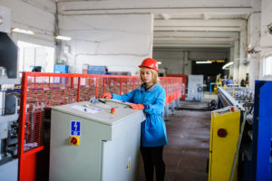 woman in red safety helmet work as industrial worker at metal sheet profiling mechine at manufacturing factory
